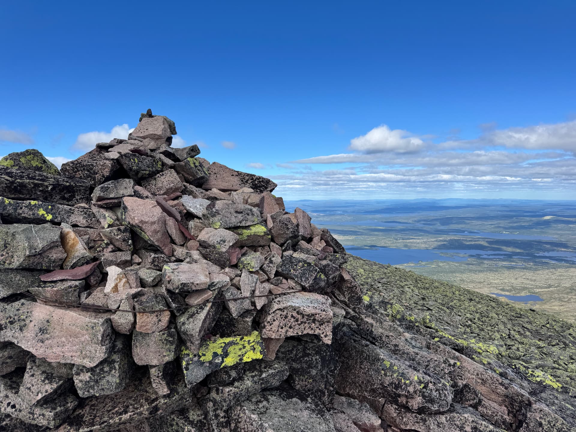 Summit cairn on Sølentoppen with lichen-covered rocks and distant blue mountains and lakes on the horizon